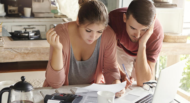 Young Married Couple With Many Debts Doing Paperwork Together, Reviewing Their Bills, Planning Family Budget And Calculating Finances At Kitchen Table With Papers, Calculator And Laptop Computer
